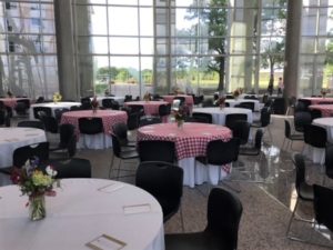 The AgriLife Center set up for an event. Multiple tables with white table cloths and red and white checkered table cloths are spread throughout the room. Each table has a flower arrangement sitting in the middle.