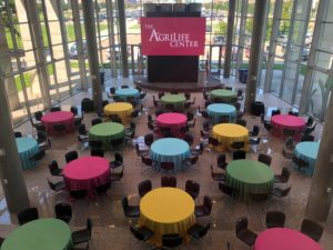 The AgriLife Center set up for an event. There are multiple tables with chairs set up. There are red, blue, green, and yellow table cloths alternating on each table. The screen has the words "The AgriLife Center" displayed.