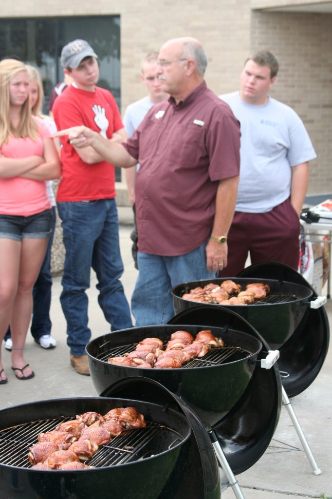 Jeff Savell teaches students about BBQ next to three BBQs with meat.
