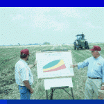 Men in field instructing others by displaying a pie chart